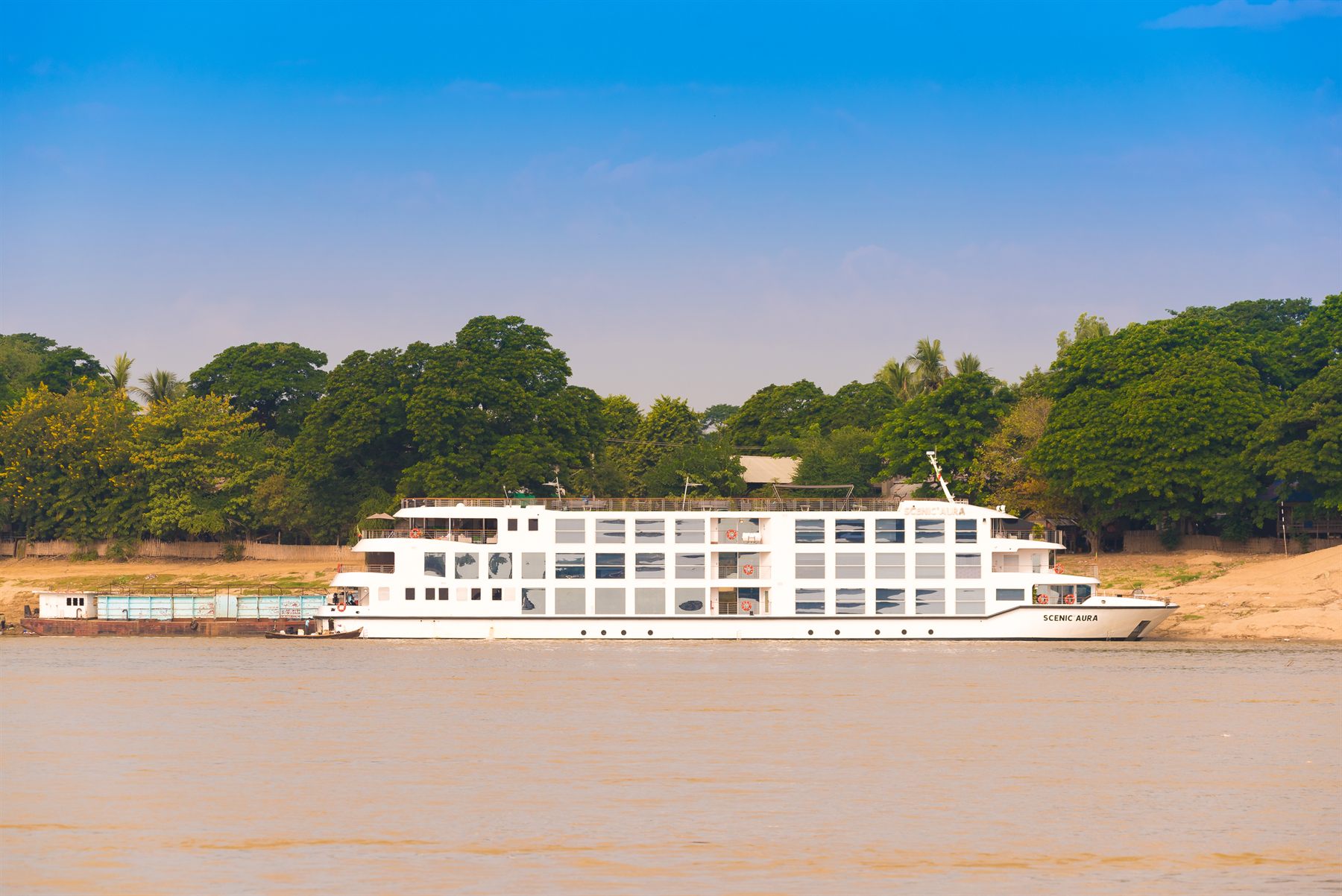The river cruise ship Scenic Aura moored against a sandy, tree-lined bank of the Irrawaddy